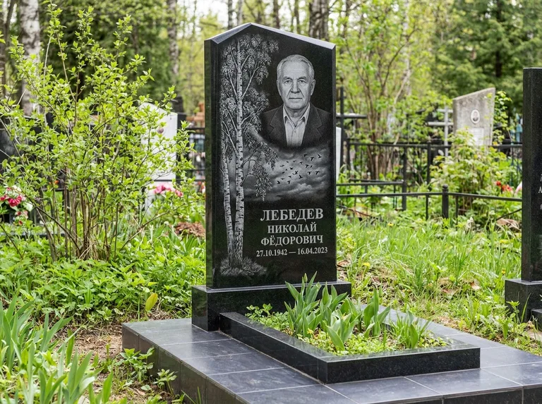 Памятник с гравировкой берёзы: вертикальная стела со скошенным верхом — берёза и стая птиц в небе, гранитный цоколь с тёмной плиткой, работа «Лебедев» в Салехарде