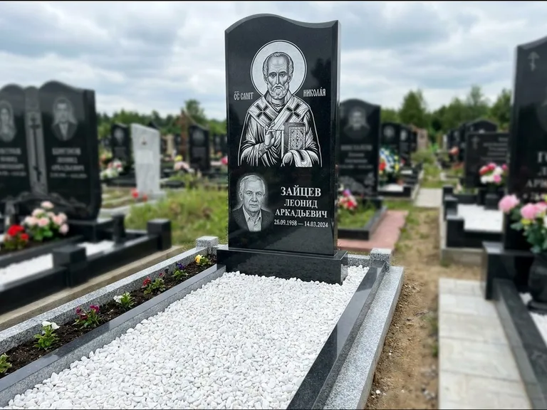 Памятник с гравировкой иконы: стела с крестообразным навершием — икона в резной рамке-киоте, газон без ограды, стриженая трава, работа «Раевская» в Салехарде