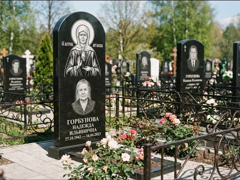 Памятник с гравировкой иконы: стела с арочным верхом и киотом под образ — гравировка образа Матроны Московской, гранитный цоколь с тёмной плиткой, работа «Ковалёв» в Салехарде