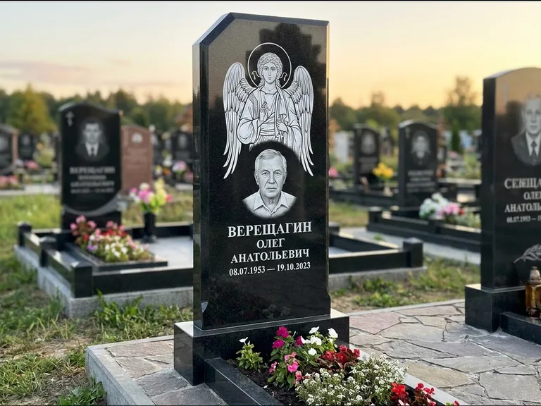Памятник с гравировкой иконы: стела с резным навершием и нимбом в золоте — гравировка образа Спасителя, высокие разросшиеся туи полукругом, работа «Мельникова» в Салехарде