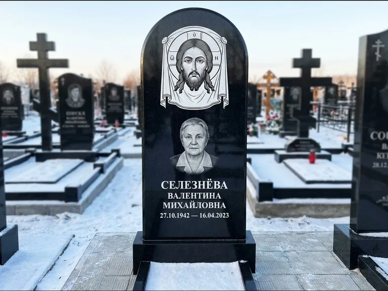 Памятник с гравировкой иконы: небольшая скромная одиночная стела с именной иконой — золочёный нимб на образе, аккуратный участок с газоном, работа «Ковалёв» в Салехарде