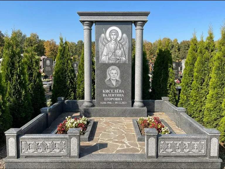 Памятник с гравировкой иконы: массивная стела с двускатным навершием-домиком — гравировка Николая Чудотворца, живая изгородь из туи, работа «Журавлёв» в Салехарде