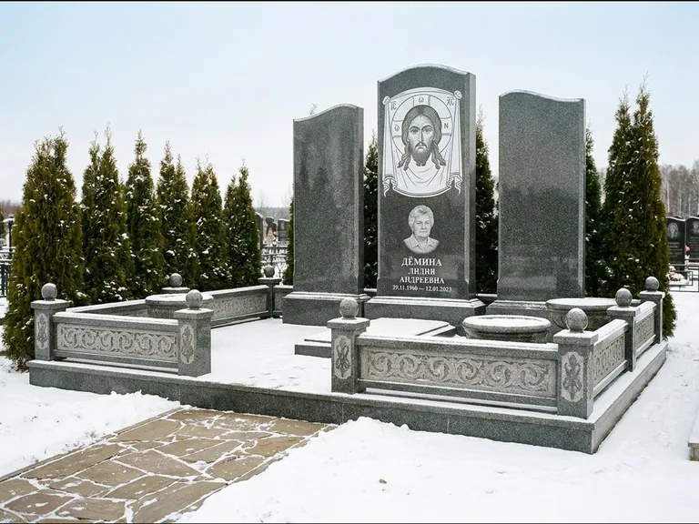 Памятник с гравировкой иконы: узкая вертикальная стела-пилон с ликом — икона в резной рамке-киоте, открытая лужайка без ограды, работа «Одинцов» в Салехарде