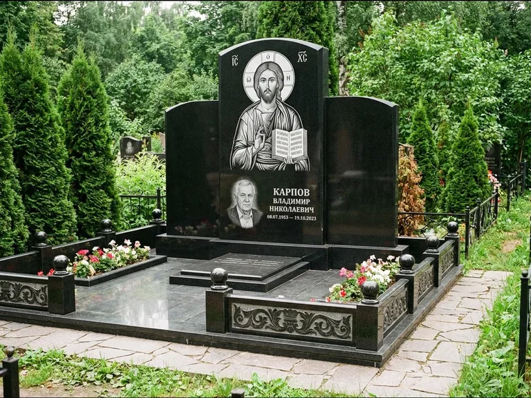 Памятник с гравировкой иконы: широкая панорамная стела с золочёным нимбом — гравировка образа Матроны Московской, цветник с белыми хризантемами, работа «Мельникова» в Салехарде