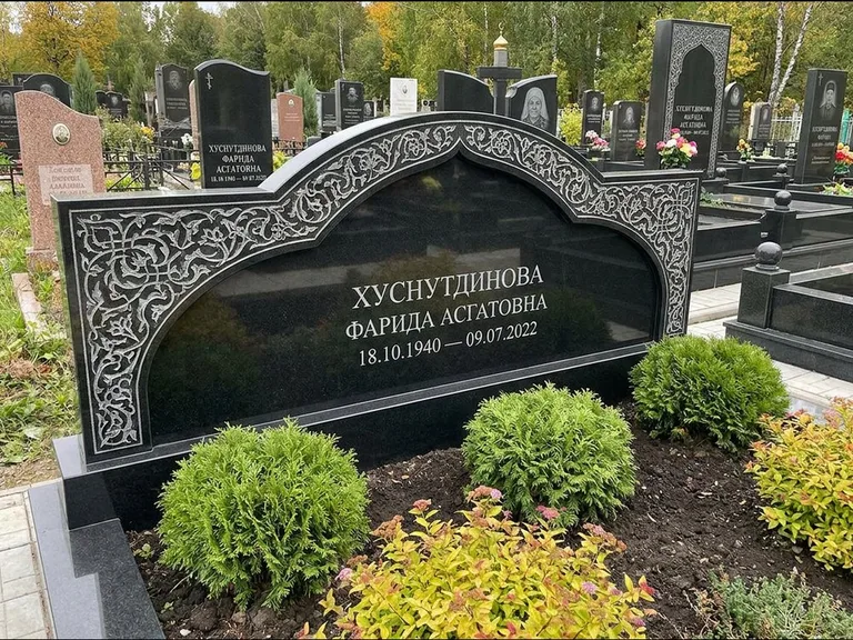 Мусульманский памятник: вытянутая горизонтальная семейная стела с аркой — белая гравировка силуэта мечети с минаретами, участок с декоративными кустами, работа «Зарипова» в Салехарде