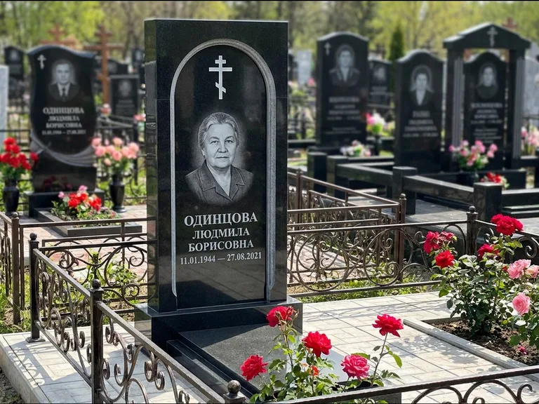 Памятник из чёрного гранита — скромная невысокая стела с крестом с терновым венцом, работа «Лаврентьева» в Салехарде